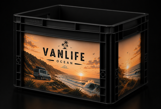 Schwarze Auer Eurobox 40 × 30 × 27 cm mit passgenauem Vanlife Ocean Sticker-Set. Das Motiv zeigt einen Campervan an einer Küste bei Sonnenuntergang mit Wellen, Steilküste und Palmen im Vintage-Look. Die Aufkleber sind sauber auf der Front- und Seitenfläche angebracht und werden in einer hellen Studioaufnahme präsentiert.